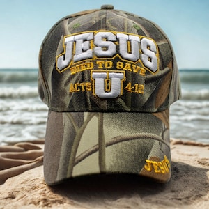 May include: Camouflage baseball cap featuring the embroidered text "JESUS DIED TO SAVE ACTS U 4:12" in white and gold. The cap is on a sandy beach with the sea in the background.