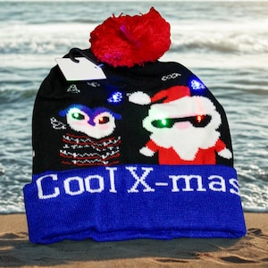 May include: Black Christmas beanie with a blue brim and a red pom-pom. The hat features a design with a Santa Claus and an owl, both with glowing LED lights. The text "Cool X-mas" is displayed on the brim.