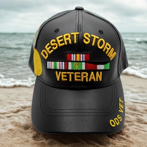 Puede incluir: Gorra de béisbol negra con la inscripción dorada "DESERT STORM VETERAN". La gorra presenta cintas militares y el texto "ODS VET" en la visera. Una medalla de oro está en el lateral.