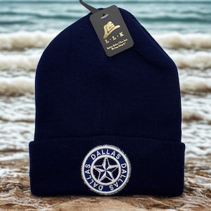 May include: A navy blue knit beanie with a white and silver Dallas star logo. The beanie has a folded brim and a tag with the letters "L.L.K." and the text "Better. Better Than Best. We keep being it!"