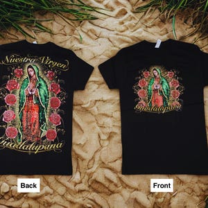 May include: Two black t-shirts with a graphic of the Virgin of Guadalupe. The front of the shirt has the image with the text "Guadalupana". The back of the shirt has the image with the text "Nuestra Virgen Guadalupana".