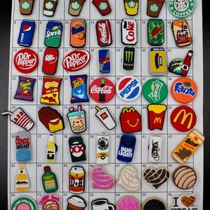 May include: A collection of colorful shoe charms featuring various food and beverage brands, including soda cans, coffee cups, and fast food logos. The charms are made of a durable material and are designed to be attached to shoes.