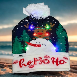 May include: A Christmas beanie hat with a snowman and reindeer design, featuring the text "Ho Ho Ho" in red. The hat has a white pom-pom and is illuminated with colourful LED lights, ideal for festive occasions.