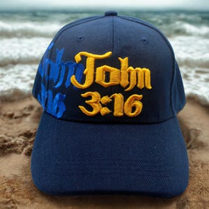 May include: Navy blue baseball cap with the text "John 3:16" embroidered in gold and blue. The cap is made of a durable fabric and features a curved brim. The hat is a classic style, suitable for casual wear.