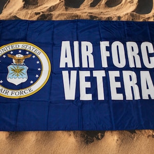 May include: A blue Air Force Veteran flag with white text and the Air Force emblem. The flag is rectangular and features the words "AIR FORCE VETERAN" in large, bold letters. The emblem is a circular design with the words "UNITED STATES AIR FORCE".