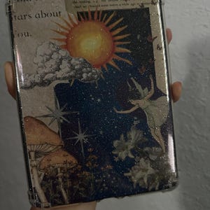 May include: Clear protective case with a whimsical design. The case features a collage of illustrations including a sun, mushrooms, stars, and a fairy. Text on the case reads "did the stars about you" and "THE STARS, SURS OF THE INFINITA".