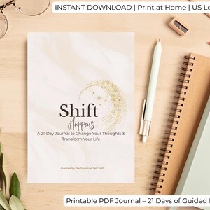 May include: A journal titled "Shift Happens" with a gold crescent moon design. The journal promises a 21-day program to change thoughts and transform life. The image also includes a pen, notebooks, and glasses, suggesting a workspace.