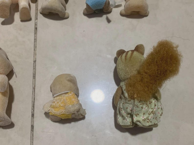 Puede incluir: Una colecci&oacute;n de figuras de animales en miniatura. Una figura de ardilla est&aacute; en foco, con una cola marr&oacute;n esponjosa y usando un peto con un estampado floral. Otras figuras incluyen un beb&eacute; con pa&ntilde;al y otros animales.