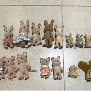 Puede incluir: Una colecci&oacute;n de figuras de animales en miniatura, incluyendo conejos, ratones y ardillas. Los conejos est&aacute;n en varios colores y atuendos, algunos con vestidos y monos. Los ratones y las ardillas tambi&eacute;n est&aacute;n vestidos con ropa en miniatura. Las figuras est&aacute;n dispuestas sobre una superficie clara.