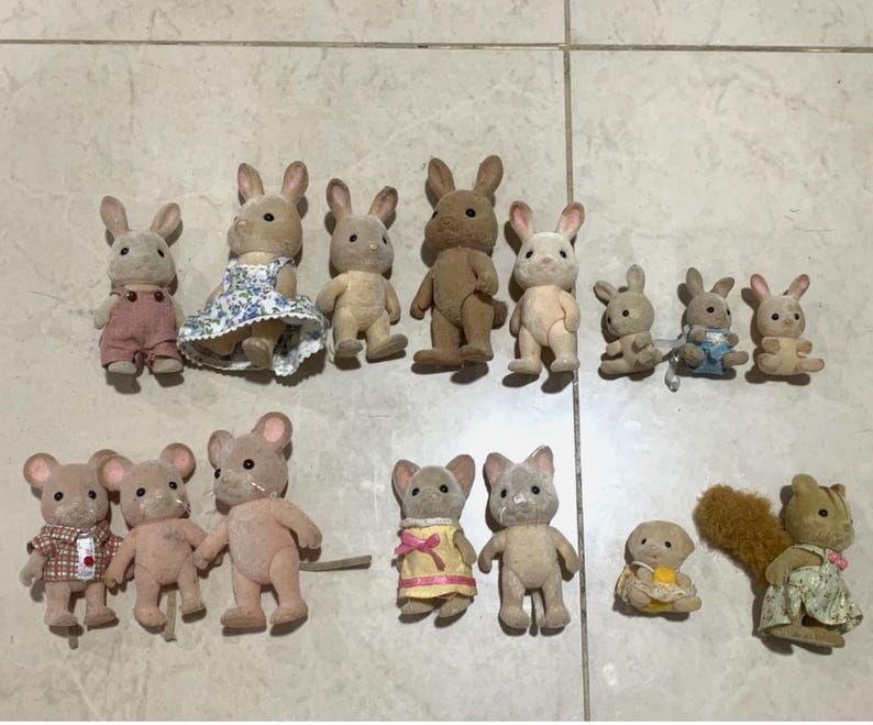 Puede incluir: Una colecci&oacute;n de figuras de animales en miniatura, incluyendo conejos, ratones y ardillas. Los conejos est&aacute;n en varios colores y atuendos, algunos con vestidos y monos. Los ratones y las ardillas tambi&eacute;n est&aacute;n vestidos con ropa en miniatura. Las figuras est&aacute;n dispuestas sobre una superficie clara.