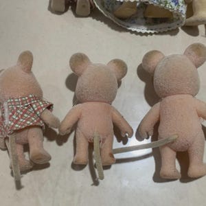 Puede incluir: Tres peque&ntilde;as figuras de rat&oacute;n rosas con texturas difusas. Un rat&oacute;n lleva una camisa a cuadros rojos y blancos. Cada rat&oacute;n tiene una cola larga de color claro. Las figuras son parte de un juego de juguetes.