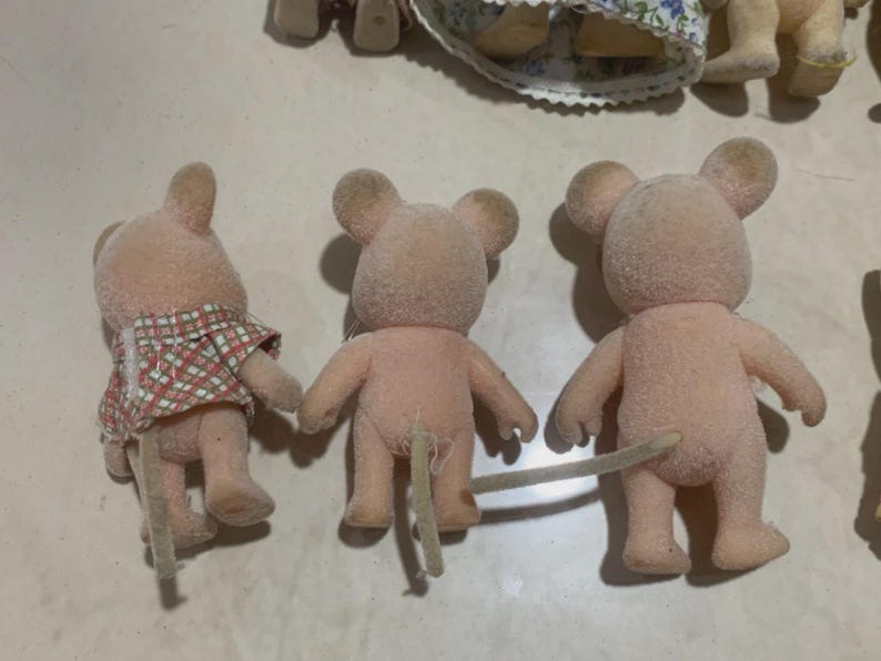 Puede incluir: Tres peque&ntilde;as figuras de rat&oacute;n rosas con texturas difusas. Un rat&oacute;n lleva una camisa a cuadros rojos y blancos. Cada rat&oacute;n tiene una cola larga de color claro. Las figuras son parte de un juego de juguetes.