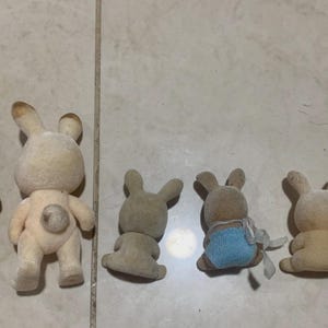Puede incluir: Colecci&oacute;n de peque&ntilde;as figuras de conejos flocados en varias poses. Los conejos son principalmente beige y marr&oacute;n, algunos con detalles azules. Las figuras tienen una est&eacute;tica vintage, con detalles como orejas y colas esponjosas.