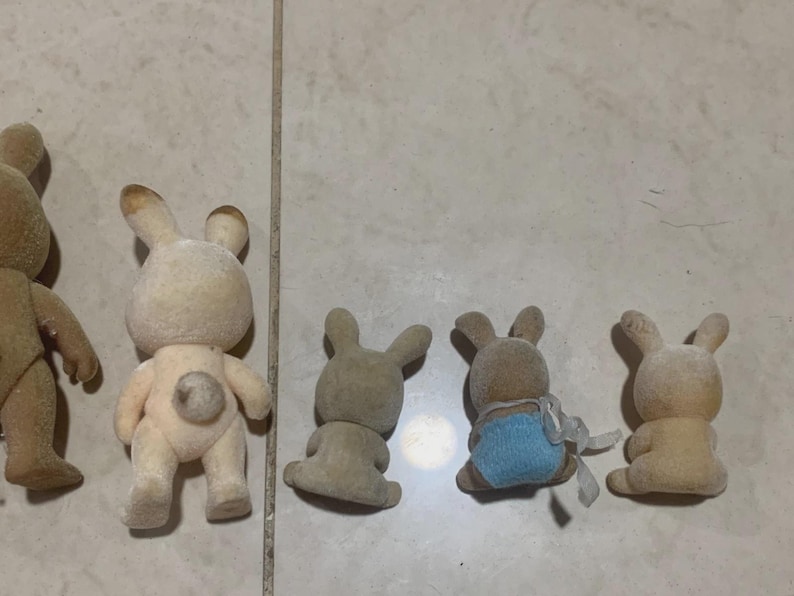 Puede incluir: Colecci&oacute;n de peque&ntilde;as figuras de conejos flocados en varias poses. Los conejos son principalmente beige y marr&oacute;n, algunos con detalles azules. Las figuras tienen una est&eacute;tica vintage, con detalles como orejas y colas esponjosas.