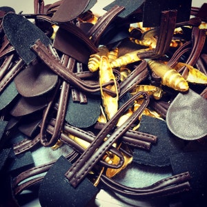 Pode incluir: Um close-up de um monte de tiras de couro marrom e peças de metal douradas. As tiras estão entrelaçadas e sobrepostas, criando um design texturizado e intrincado.