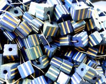 May include: A pile of blue and yellow striped wooden beads. The beads are square shaped and have a hole in the centre. The beads are strung together on a white string.