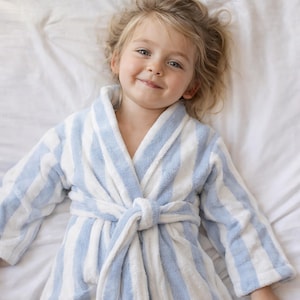 May include: A light blue and white striped bathrobe with a matching belt. The robe is made of a soft, plush material. The bathrobe is shown on a white bed.