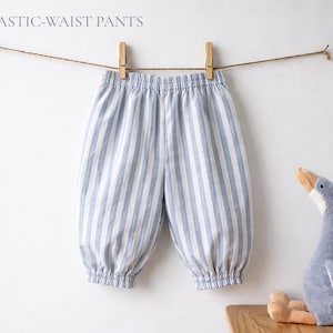 May include: Pants with a light blue and white vertical striped pattern, featuring an elastic waistband and elasticized cuffs at the ankles. The text COMFY ELASTIC-WAIST PANTS is visible at the top left. A plush goose toy is positioned nearby.
