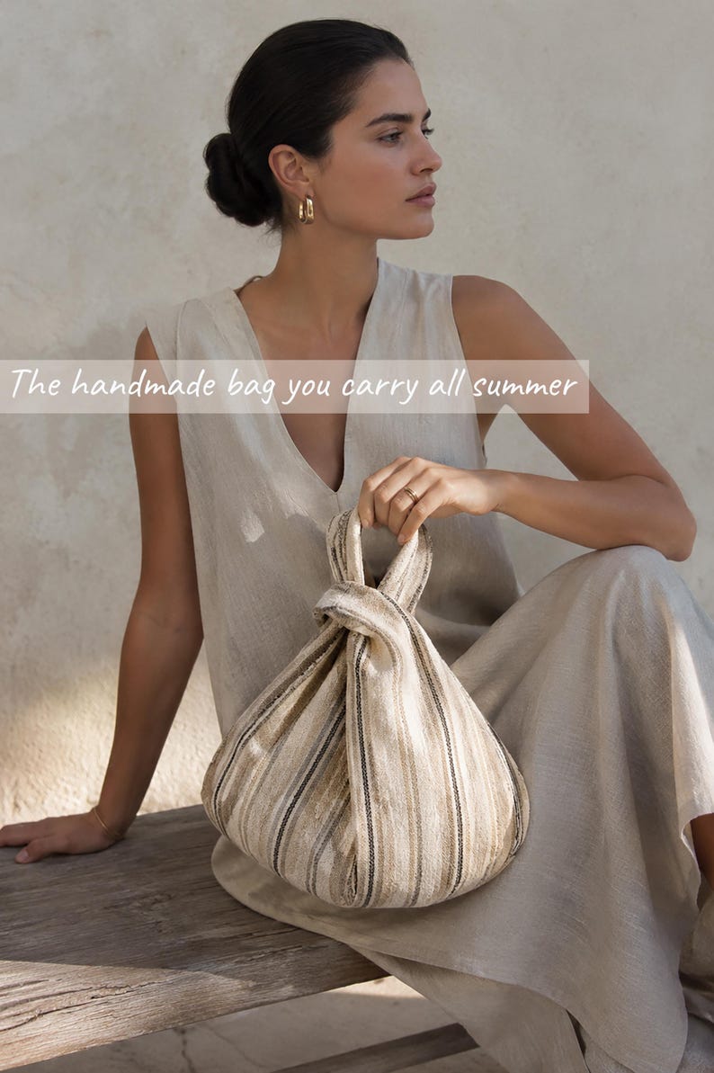 May include: A beige and brown striped fabric bag with a knotted handle design. The bag features vertical stripes in varying shades of tan, cream, and dark brown. The text "The handmade bag you carry all summer" is overlaid across the center of the image.