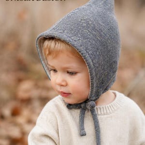 May include: A grey speckled pointed bonnet with a light-colored interior lining and tie closures under the chin. The text A TIMELESS, UNISEX DESIGN is visible in the upper left corner of the image. The bonnet features a textured fabric finish.