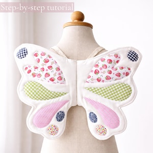 May include: Fabric butterfly wings featuring white base fabric with quilted sections of strawberry, green gingham, pink striped, and floral patterns. The wings include small circular accents in navy gingham and floral prints, with the text "Beginner-friendly" and "Step-by-step tutorial" visible at the top.