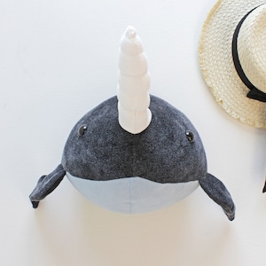 May include: A plush narwhal toy with a grey and blue body and a white curled horn. The toy has black eyes and a white belly.