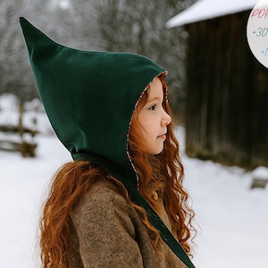 May include: A child wearing a dark green pointed hood with a red patterned lining. The hood is part of a brown coat. The image includes text that reads "PDF PATTERN +30 PICTURES +15 PAGES". The background is a snowy outdoor scene.