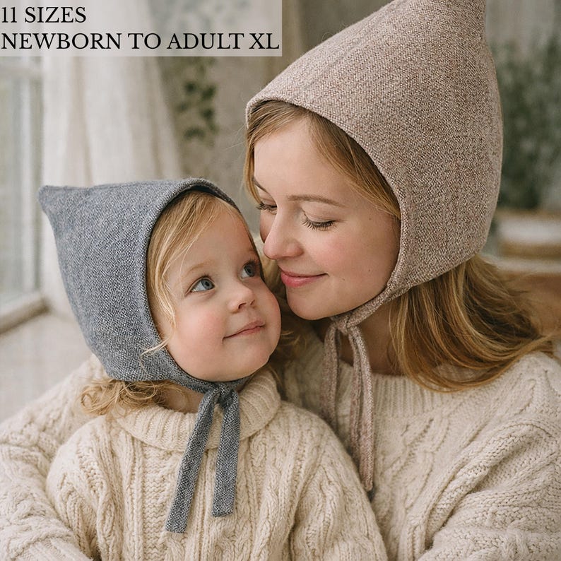 May include: Two knit bonnets with pointed tops and chin ties. One bonnet is heather gray, and the other is a light beige. The text 11 SIZES NEWBORN TO ADULT XL is visible in the upper left corner. These head coverings feature a textured knit fabric.