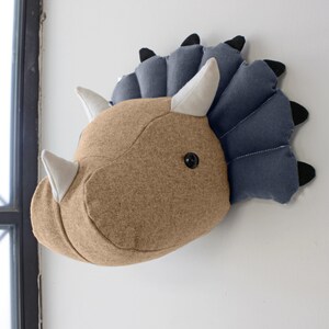 May include: A brown and blue felt dinosaur head wall hanging. The dinosaur has a large head with three horns and a frill around its neck. The horns are white and the frill is blue.