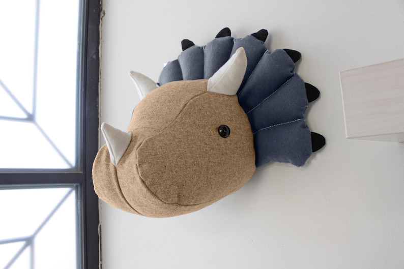 May include: A brown and blue felt dinosaur head wall hanging. The dinosaur has a large head with three horns and a frill around its neck. The horns are white and the frill is blue.