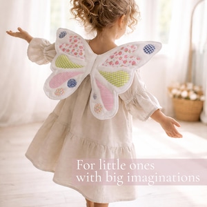 May include: Fabric butterfly wings featuring a white base with colorful patchwork sections in pink, green, and blue floral and gingham patterns. The wings are worn over a beige dress. Text on the image reads: For little ones with big imaginations.
