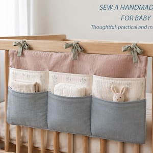 May include: A fabric crib organizer with three blue pockets and a dusty pink top section, tied to a wooden crib with green ribbons. The organizer features a floral print on the middle section and text reading SEW A HANDMADE GIFT FOR BABY.