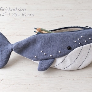 Pu&ograve; includere: Un astuccio a forma di balena in tessuto blu e bianco con chiusura a zip. L'astuccio presenta piccole perline bianche decorative e linee nere cucite sulla parte inferiore bianca. La dimensione finita &egrave; di 25 cm per 10 cm.