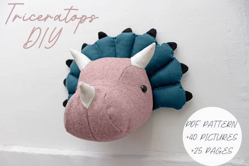 May include: A DIY Triceratops head wall decor pattern with 40 pictures and 25 pages. The pattern includes a pink felt head with white horns and a teal felt frill.