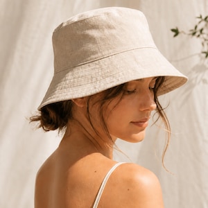 Puede incluir: Un sombrero de pescador beige con ala ancha. El sombrero está hecho de una tela texturizada y lo lleva una persona. El texto "Bucket Hat" y "PDF sewing Pattern" es visible en la imagen.