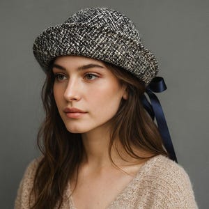 May include: A tweed cloche hat in black, white, and beige with a dark blue ribbon bow. The hat features a rounded crown and a slightly wider brim. The hat is made of a textured fabric.
