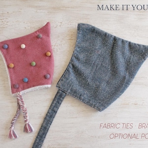 May include: A dusty rose bonnet with multicolored felt pom-poms and braided ties, alongside a charcoal gray bonnet with fabric ties. The text reads MAKE IT YOUR OWN, FABRIC TIES, BRAIDED TIES, and OPTIONAL POM-POMS.
