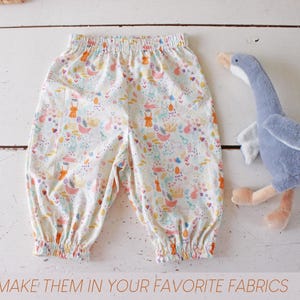 May include: A pair of white pants with an elastic waistband and cuffs, featuring a colorful pattern of small rabbits, flowers, and abstract shapes, accompanied by a plush grey goose toy. The text at the bottom reads: MAKE THEM IN YOUR FAVORITE FABRICS.