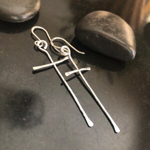 May include: A pair of silver cross earrings with a simple, minimalist design. The earrings are made of thin, twisted wire and have a delicate, openwork look.