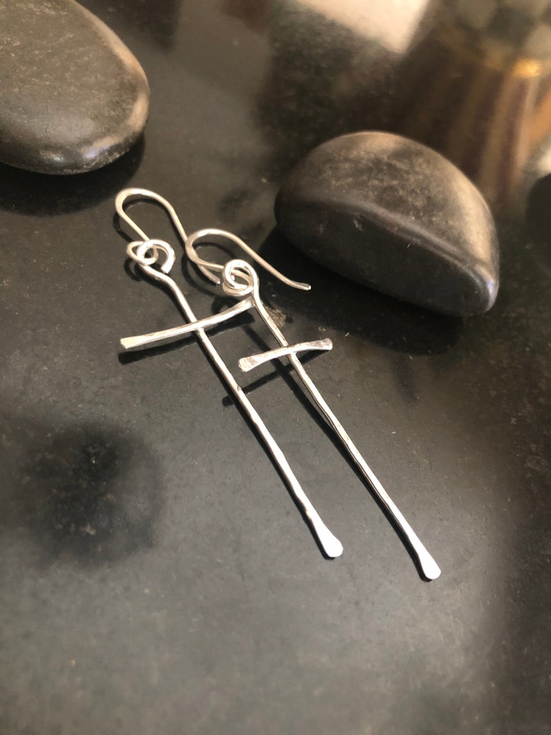 May include: A pair of silver cross earrings with a simple, minimalist design. The earrings are made of thin, twisted wire and have a delicate, openwork look.
