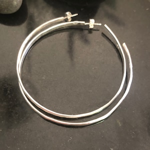 K&ouml;nnte beinhalten: Ein Paar silberne Creolen mit einem schlichten, polierten Finish. Die Ohrringe bestehen aus zwei Kreisen, wobei der eine etwas gr&ouml;&szlig;er ist als der andere, die oben miteinander verbunden sind.