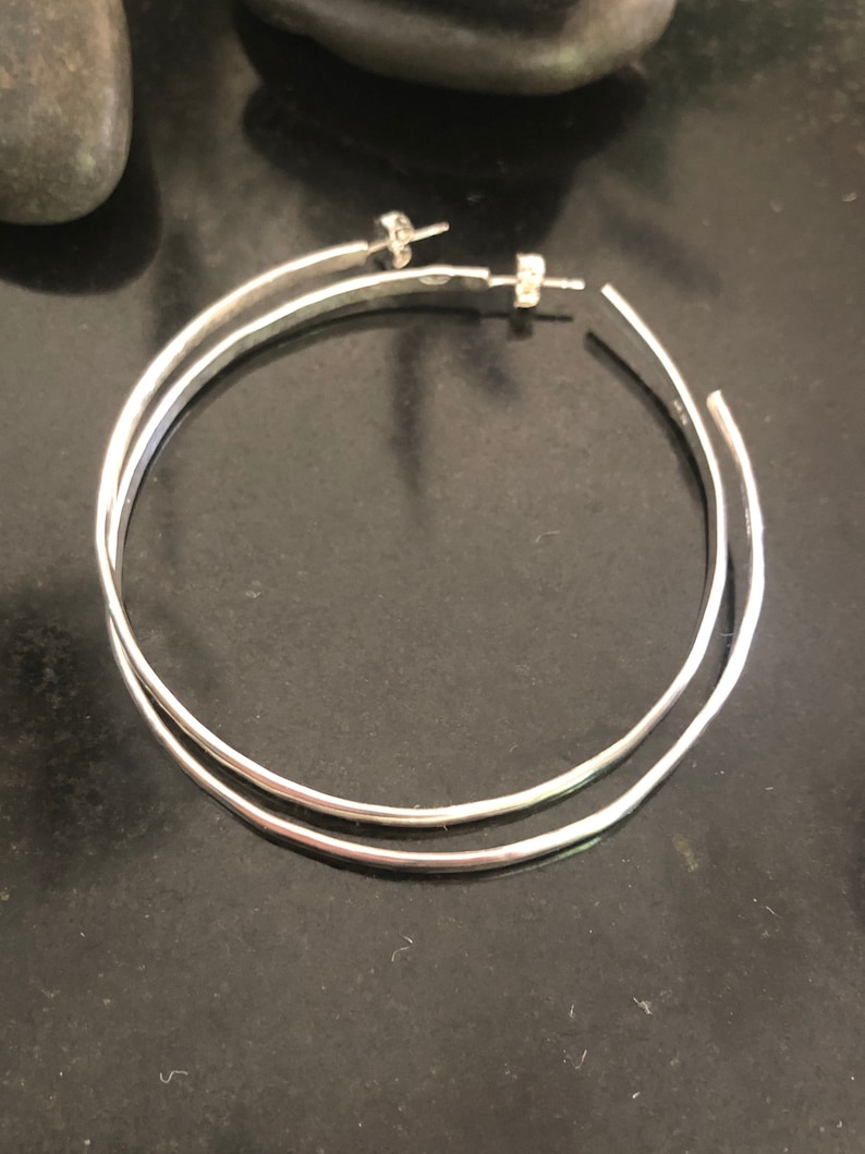 K&ouml;nnte beinhalten: Ein Paar silberne Creolen mit einem schlichten, polierten Finish. Die Ohrringe bestehen aus zwei Kreisen, wobei der eine etwas gr&ouml;&szlig;er ist als der andere, die oben miteinander verbunden sind.