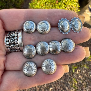 Könnte beinhalten: Eine Sammlung von acht silbernen Ohrringen mit verschiedenen floralen und geometrischen Designs. Die Ohrringe werden auf einer Hand präsentiert.