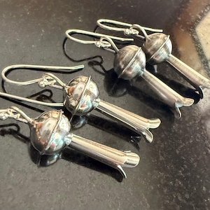 May include: Four pairs of silver earrings. Each earring has a rounded top with a textured surface and a long, slender stem ending in a flared, petal-like shape. The earrings have a hook-style closure.