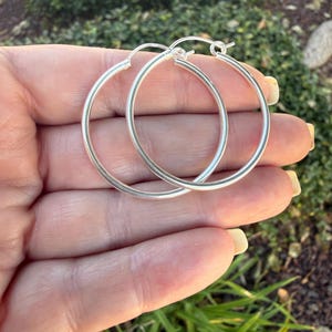 May include: A pair of polished silver hoop earrings featuring a circular, continuous design with a smooth, reflective metallic finish. The earrings are lightweight, thin, and circular in shape, showcasing a simple and clean aesthetic for everyday wear.