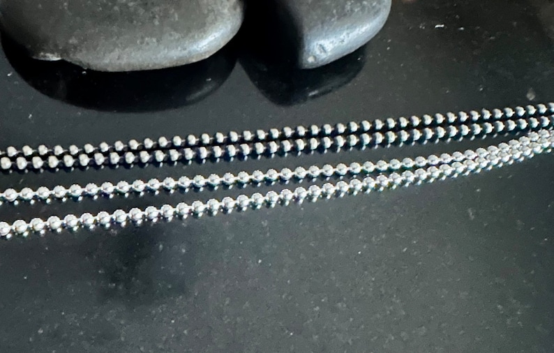 May include: Three silver chains with round beads. The chains are arranged in a row, with the top chain being the thickest and the bottom chain being the thinnest.