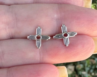 May include: Two silver-toned earrings in the shape of a stylized cross with a circle in the center. The earrings are small and delicate.