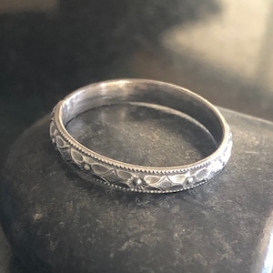 Może przedstawiać: Srebrny pierścionek z delikatnym wzorem kwiatowym. Pierścionek jest gładki i błyszczący, z subtelnym grawerowanym wzorem.