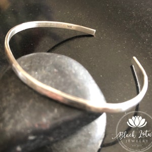 May include: A silver bangle bracelet with a hammered finish. The bracelet is marked with the number "925" on the inside.