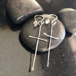 May include: A pair of silver earrings with a cross design. The earrings are made of thin wire and have a small bead at the top.